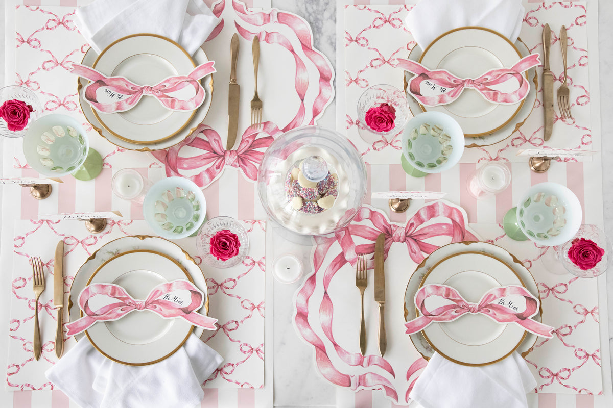 A table set for 4 with paper placemats featuring a pink bow pattern on them.  