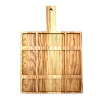 A JK Adams Ash Divided Serving Board with compartments holding pistachios, blueberries, crackers, and a dip, next to a small vase with greenery.