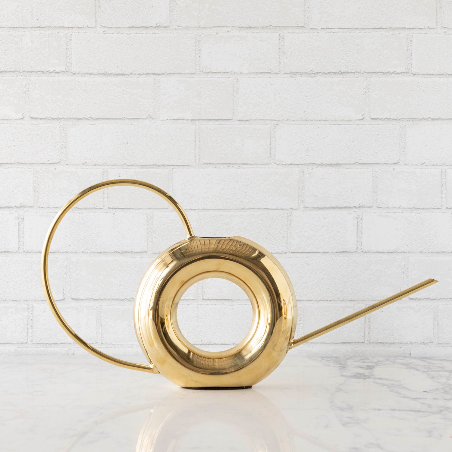 Two Accent Decor Modern Watering Cans with brass finish on a table next to flowers.