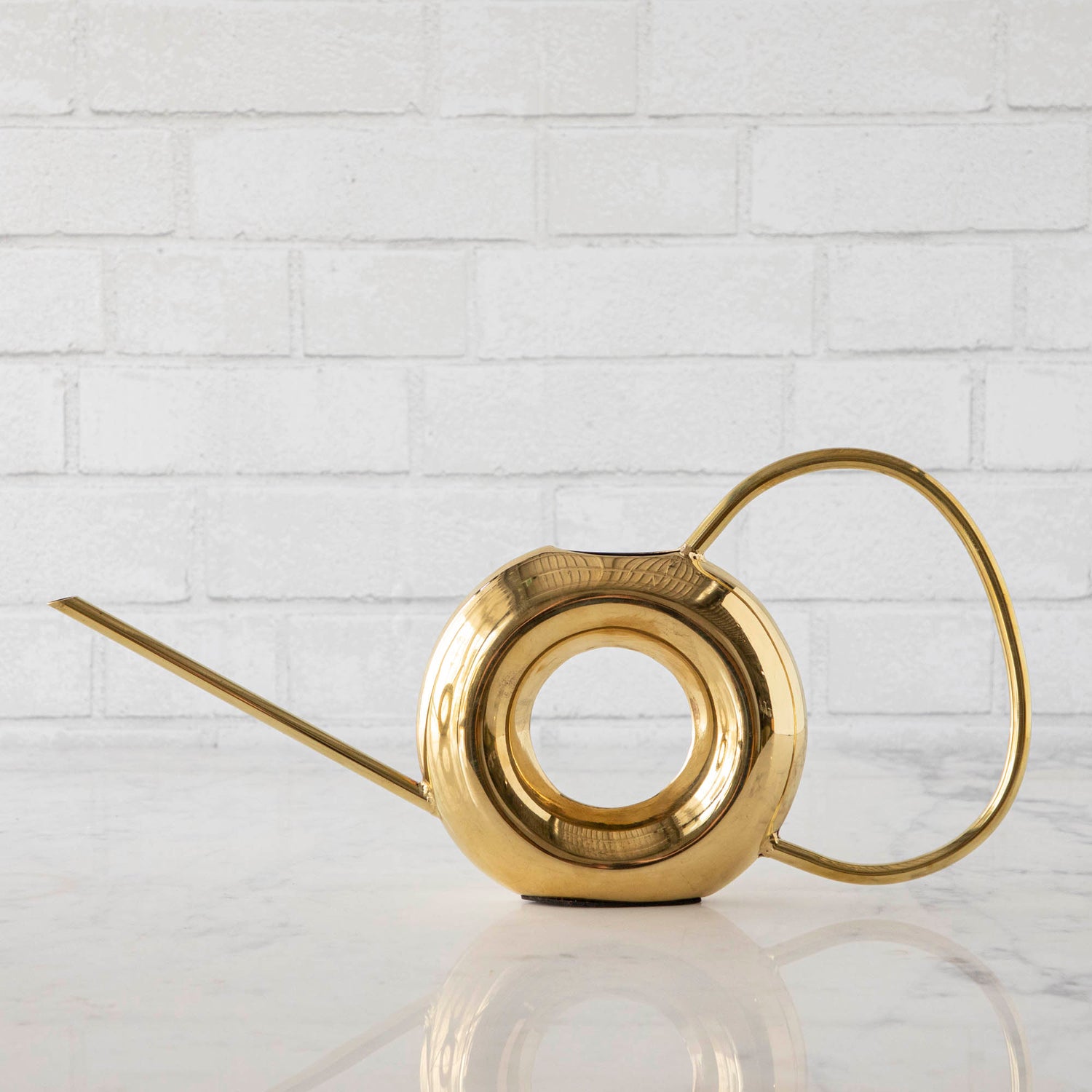 Two Accent Decor Modern Watering Cans with brass finish on a table next to flowers.