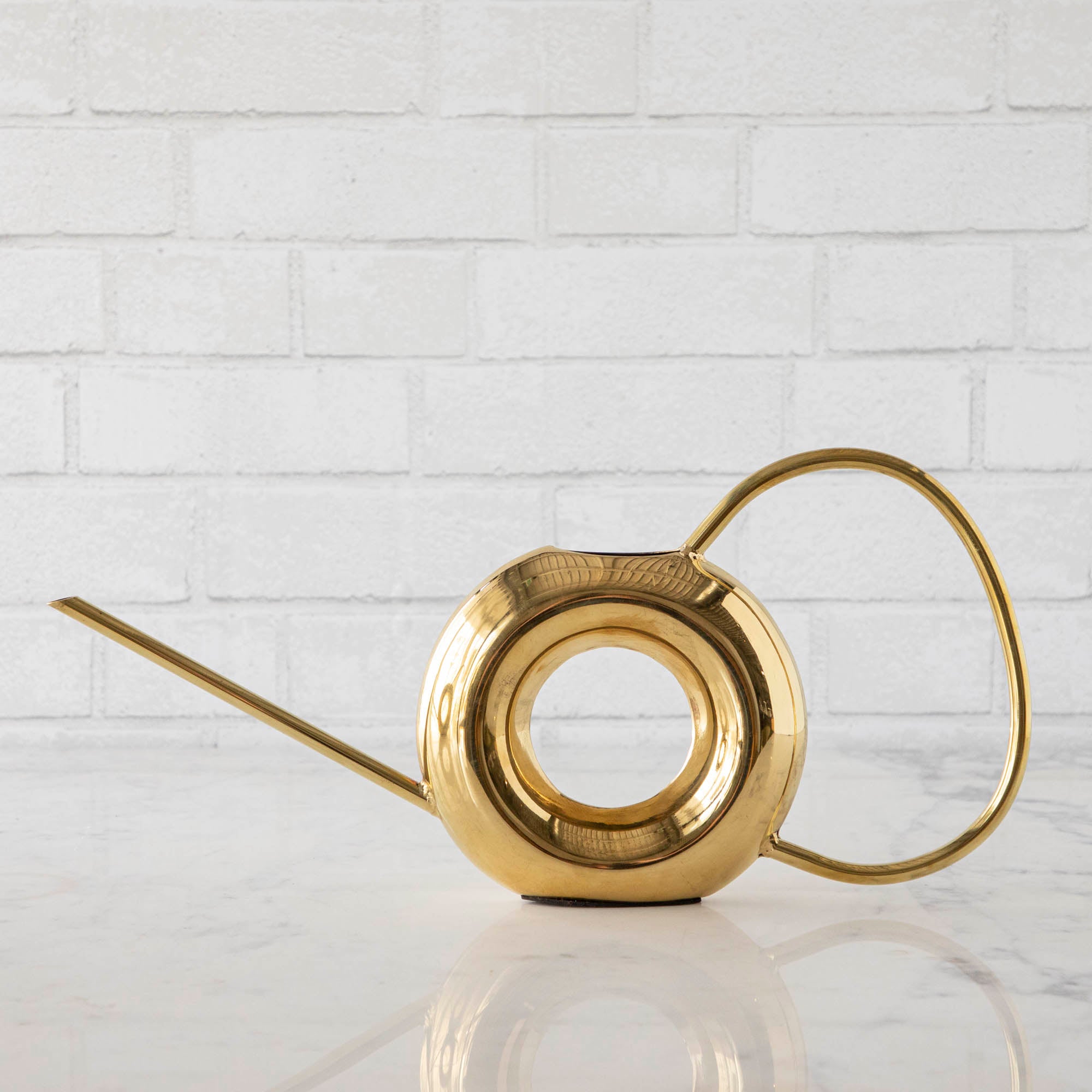 Two Accent Decor Modern Watering Cans with brass finish on a table next to flowers.