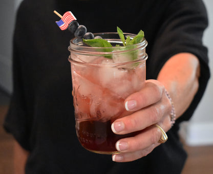 American flag cocktail pick in a cocktail with blueberries and mint. 