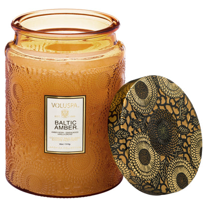 Two Voluspa Baltic Amber candles with matches on a marble surface.
