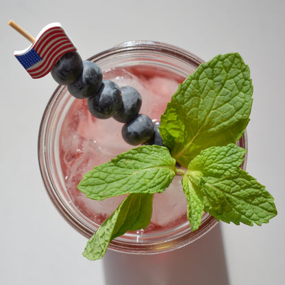 American flag cocktail pick in a cocktail with blueberries and mint. 