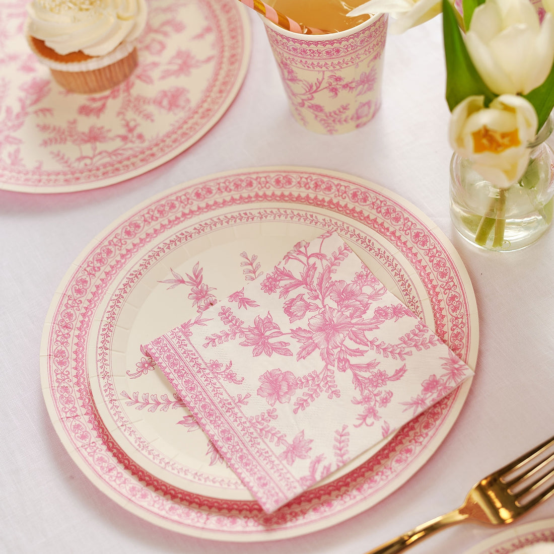 A table set with Pink French Toile Paper Party Dinnerware plates from Coterie Party Supplies featuring floral toile dinnerware patterns that evoke the charm of the French countryside, complemented by silverware.