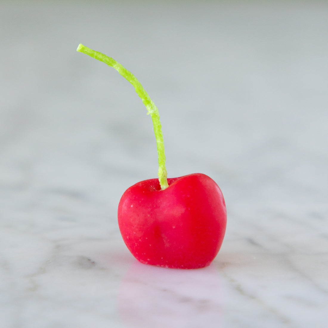 A single, cherry-shaped candle with a green stem on a marble surface.