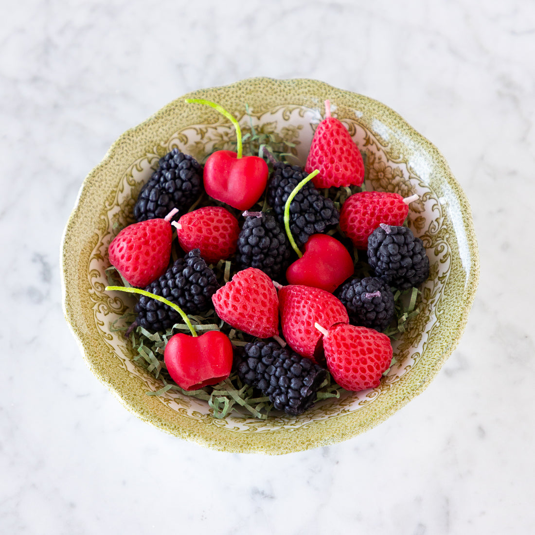 A decorative bowl filled with strawberry, blackberry and cherry shaped candles.