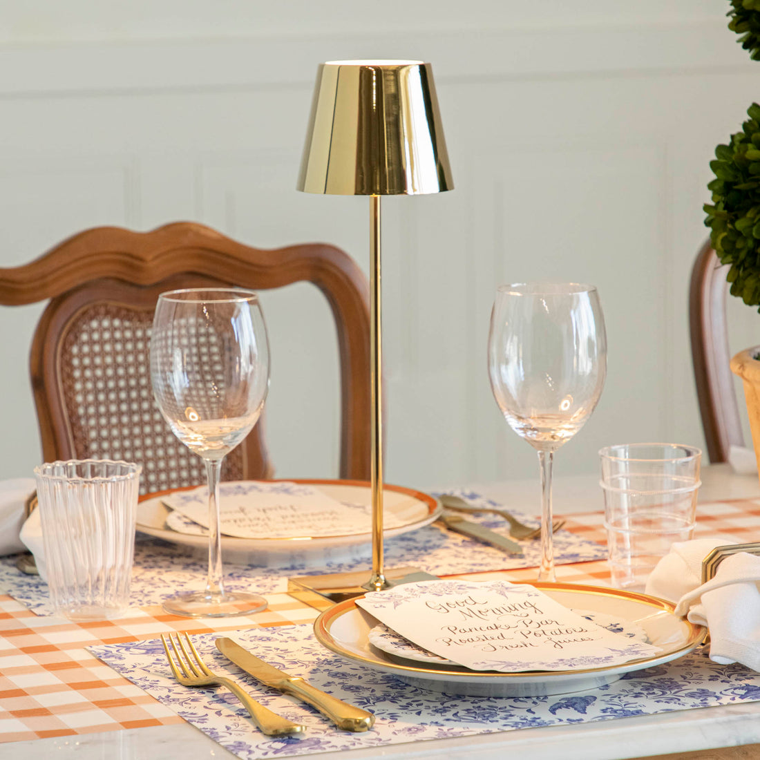 An elegantly set dining table with a modern Zafferano glossy gold cordless lamp, matching dinnerware, and glassware.