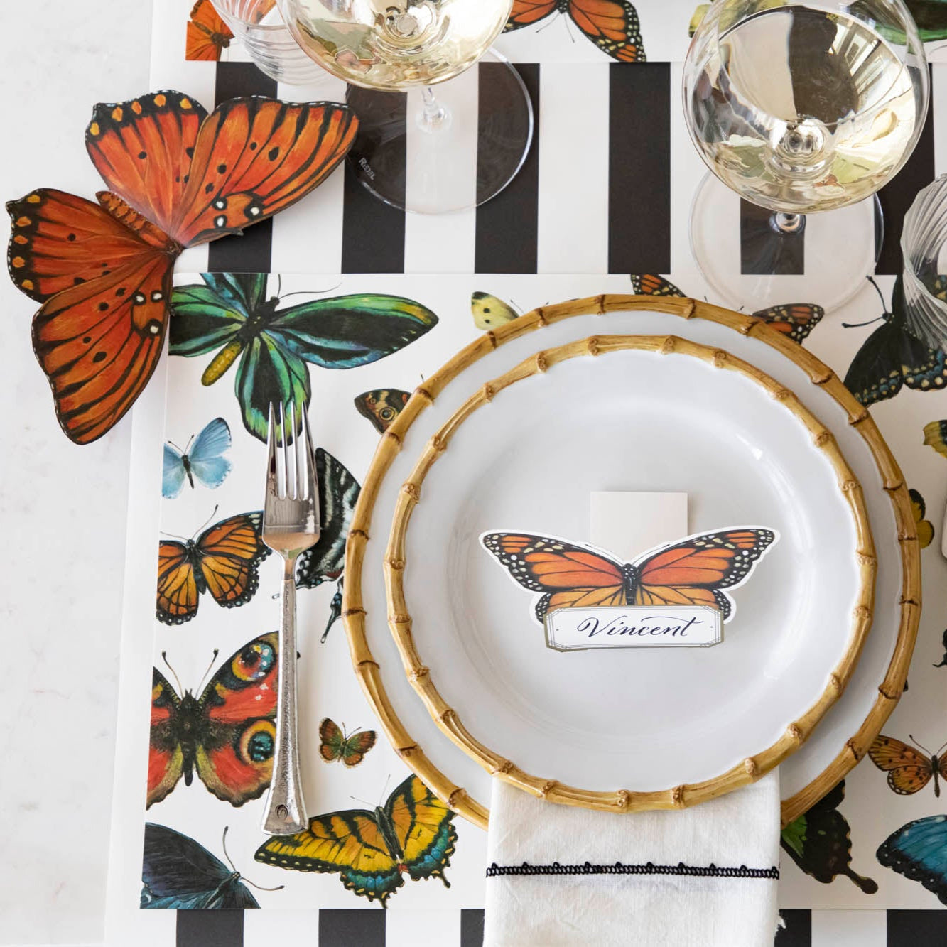 Top-down view of an elegant place setting, with the orange and green Butterfly Table Accents resting on either side of the placemat.