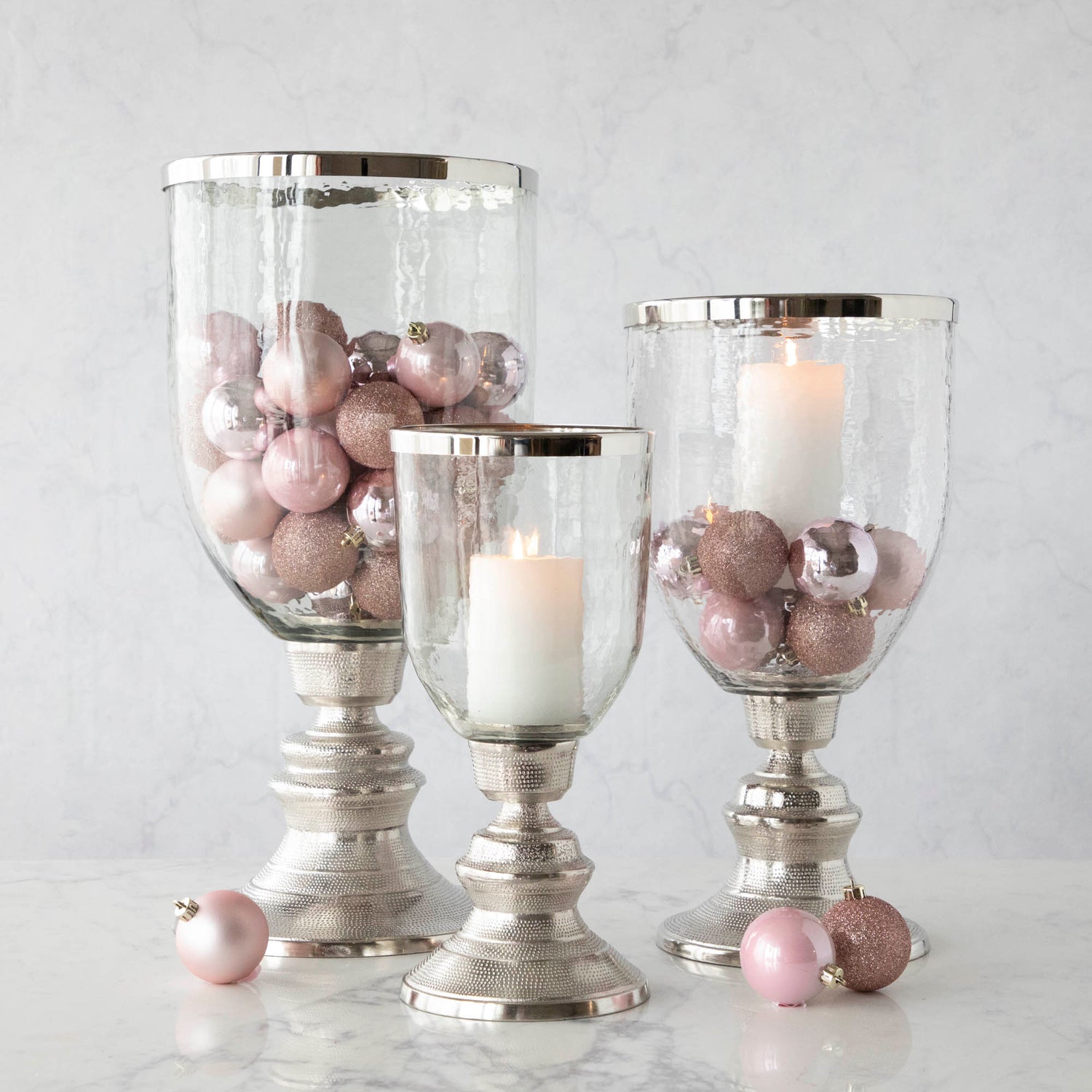 A small, medium and large Candle Hurricane Holder with a candle and pink ornaments. 