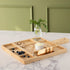 A JK Adams Ash Divided Serving Board with compartments holding pistachios, blueberries, crackers, and a dip, next to a small vase with greenery.