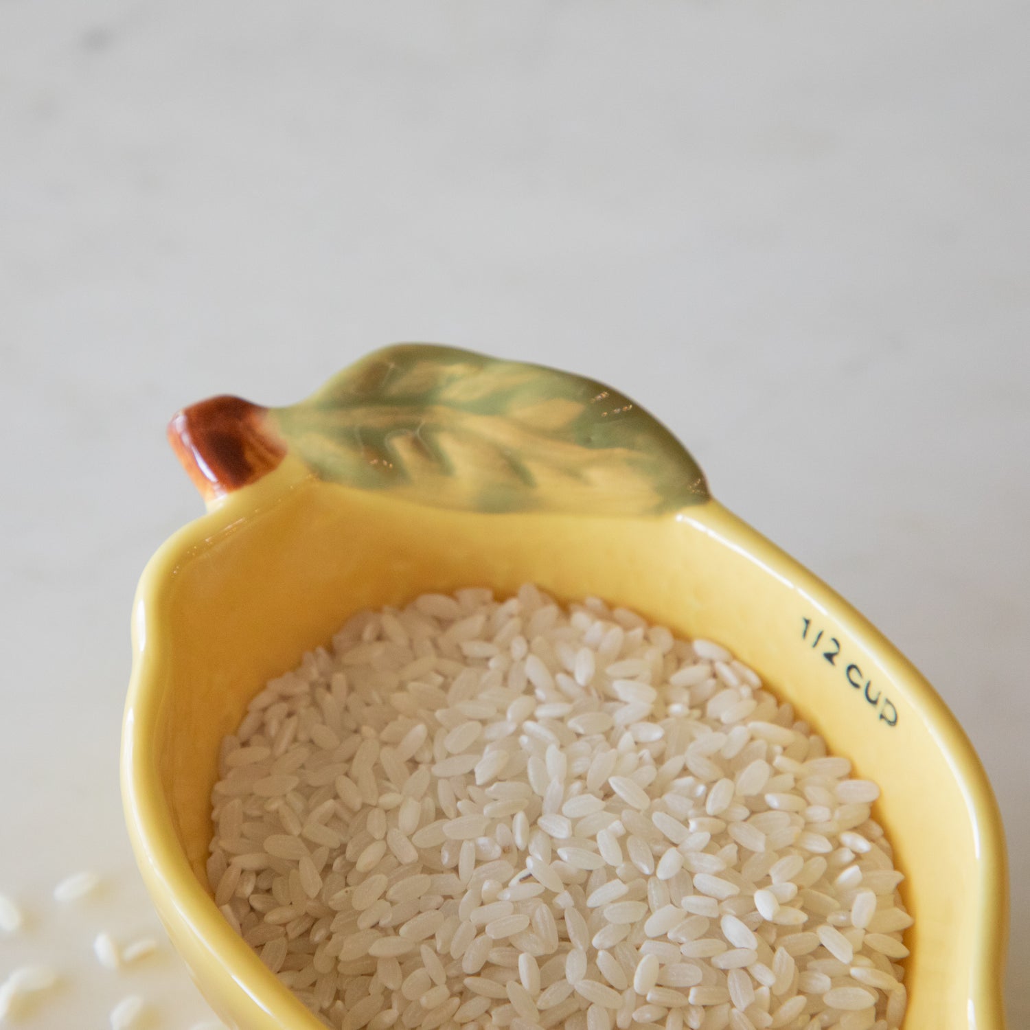 A close up view of the 1/2 lemon measuring cup showing the hand-painted green leaf on the side of the cup and rice inside.