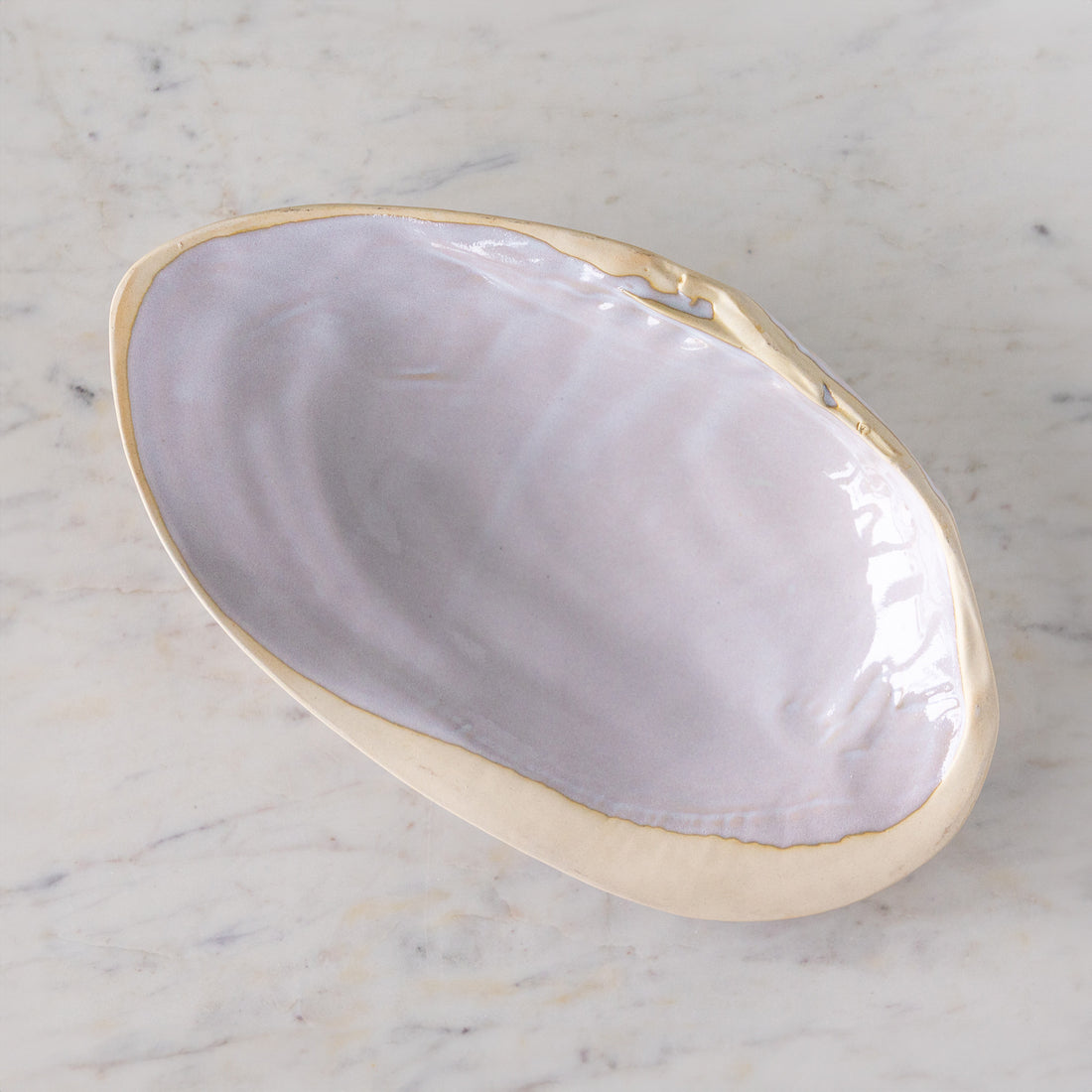 A large, oyster shell shaped dish with white reactive glaze, on a marble table.