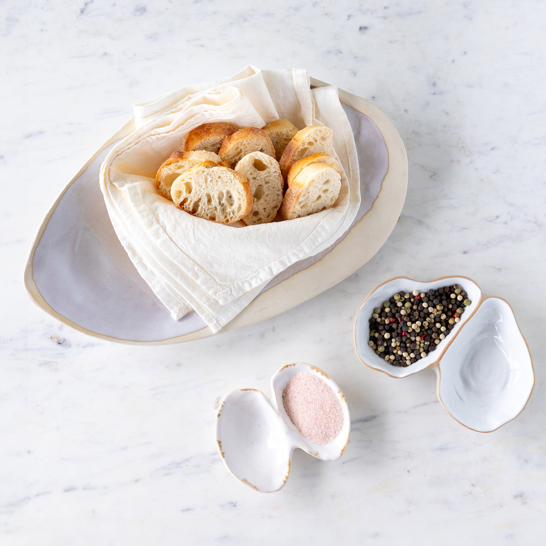 Sliced baguette on a cloth in the Single Large Oyster Shell Dish, pink salt in the Double Shell and peppercorns in the Oyster Shell.