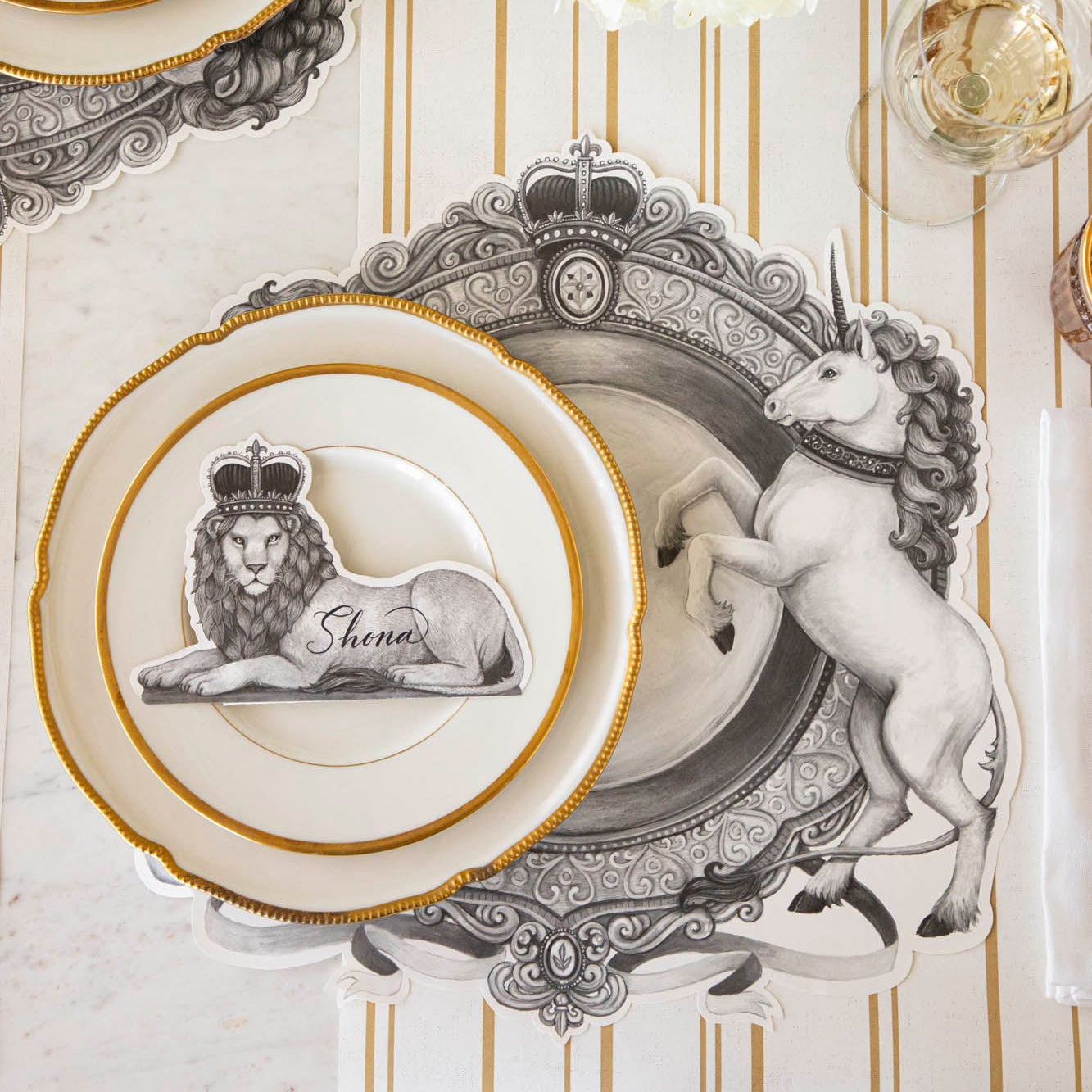 Regal Lion Place Card with "Shona" written on it, resting on dinner plates on top of the H&C Regal Crest Placemat.