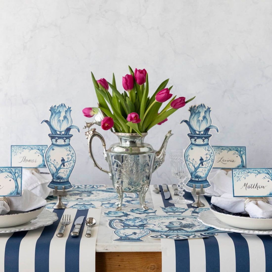 A blue and white table setting with a vase of tulips and Hester &amp; Cook vintage silver-plated tea servers.