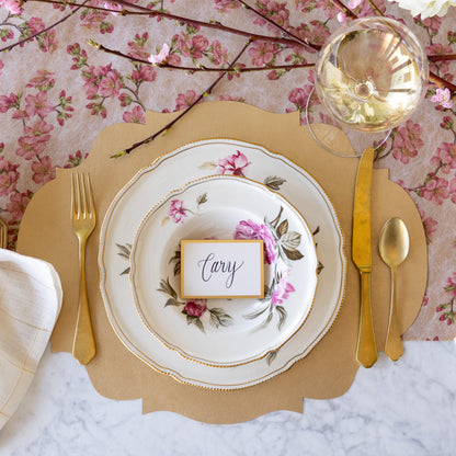 An elegant place setting featuring the Die-cut Gold French Frame Placemat, vintage dinnerware with the Gold Frame Place Card reading &quot;Cary&quot; atop, gold flatware, glass of wine, and Cherry Blossom Runner underneath.