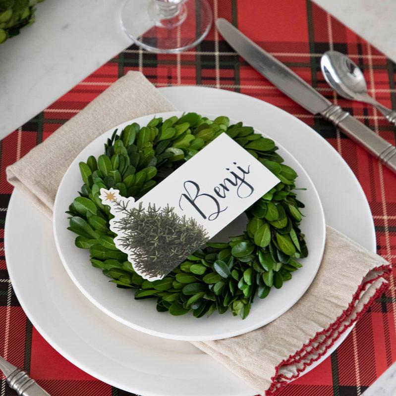 An elegant Christmastime place setting, featuring a Christmas Tree Place Card labeled &quot;Benji&quot; laying flat on the plate.