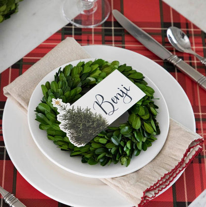 An elegant Christmastime place setting, featuring a Christmas Tree Place Card labeled &quot;Benji&quot; laying flat on the plate.