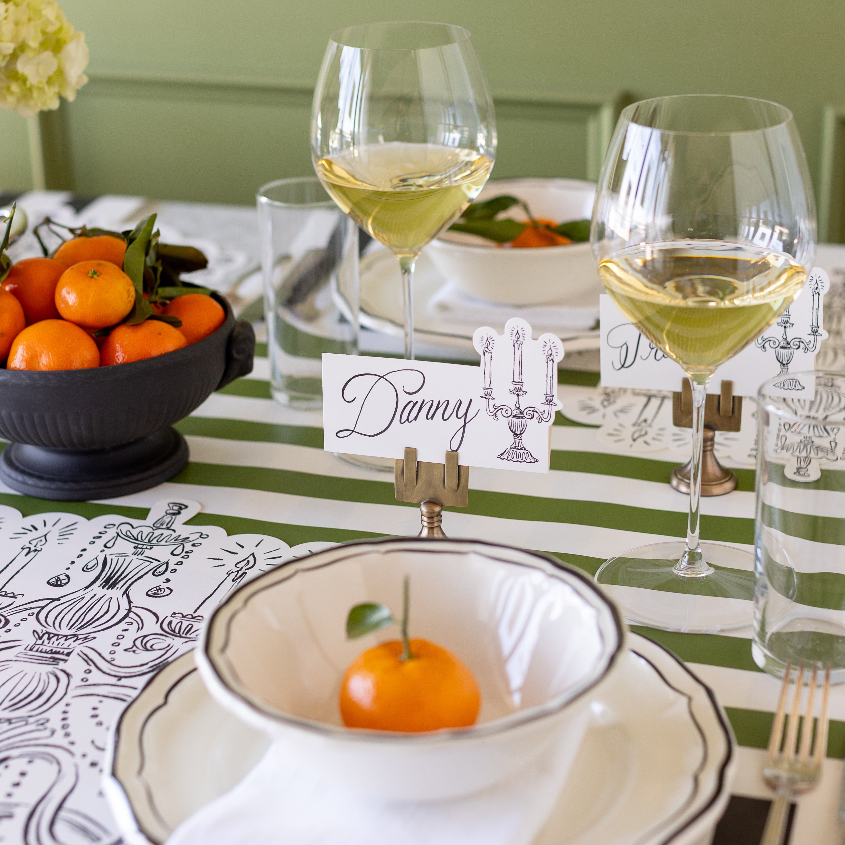 The Silver Place Card Holder holding up the Candelabra Place Card with &quot;Danny&quot; written on it, behind an elegant place setting.