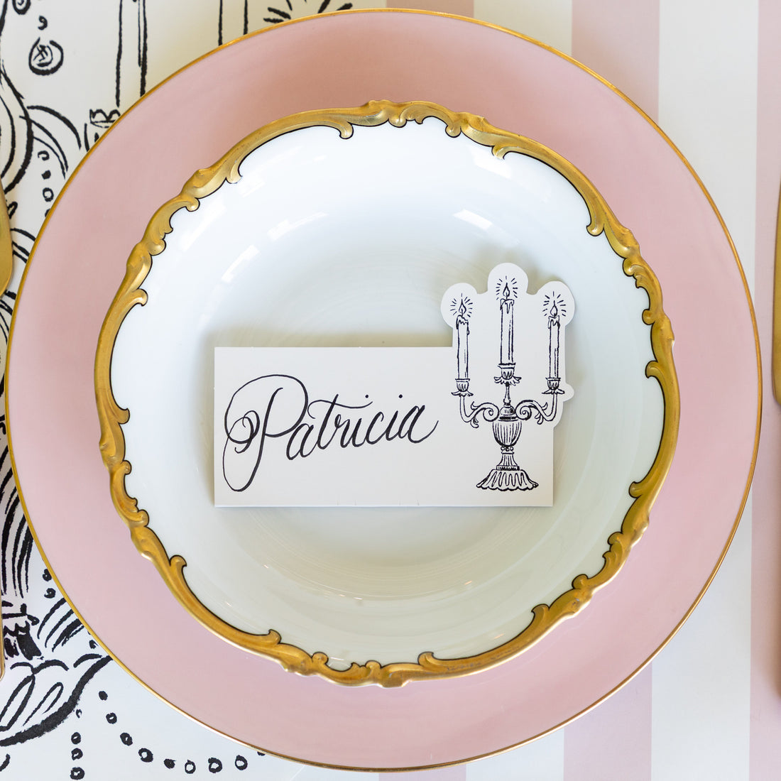 Candelabra Place Card with &quot;Patricia&quot; written on it, resting on dinner plates on a place setting.