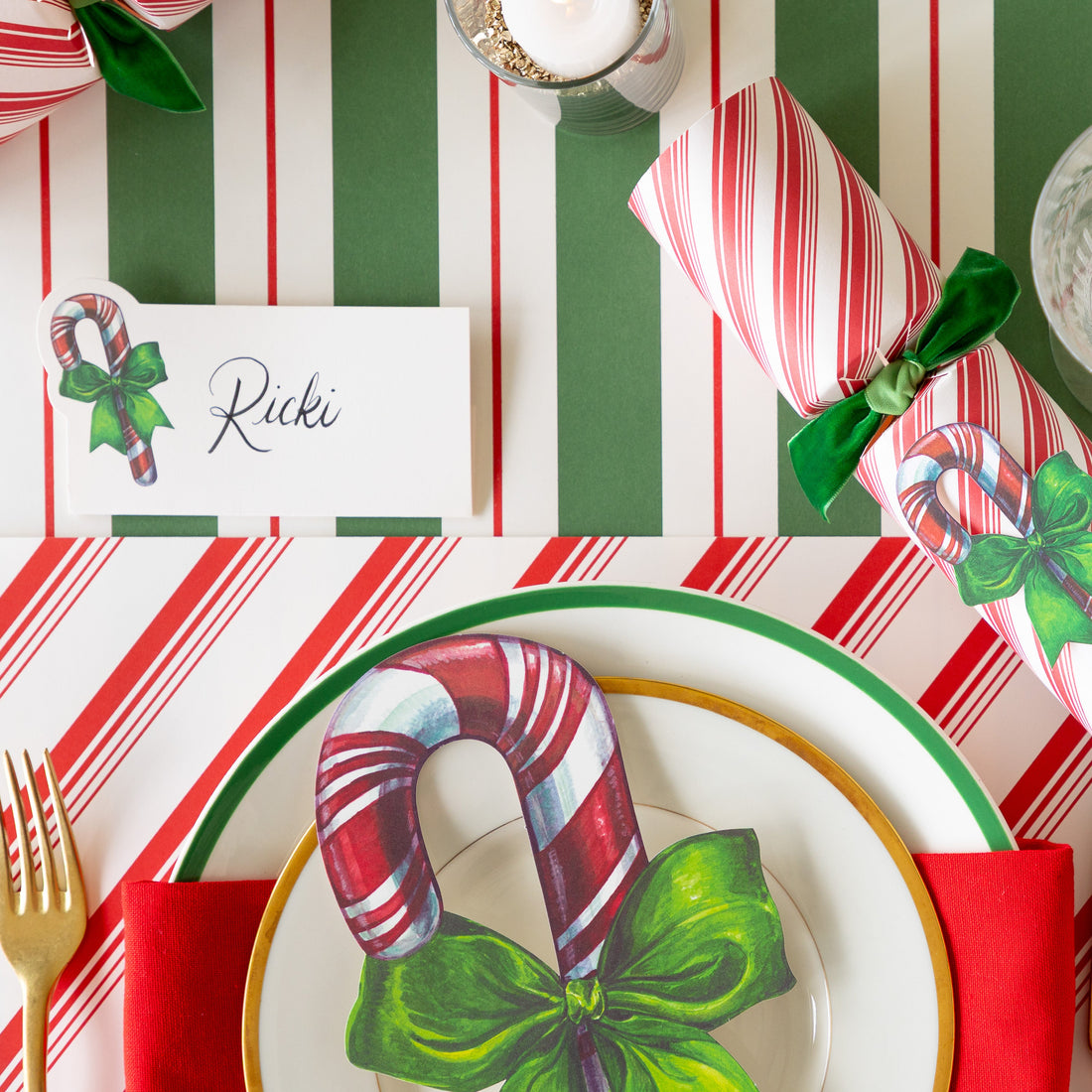 The Candy Cane Place Card reading &quot;Ricki&quot; behind a place setting featuring the Peppermint Stripe Placemat, Candy Cane Table Accent, and Green &amp; Red Awning Stripe Runner underneath.