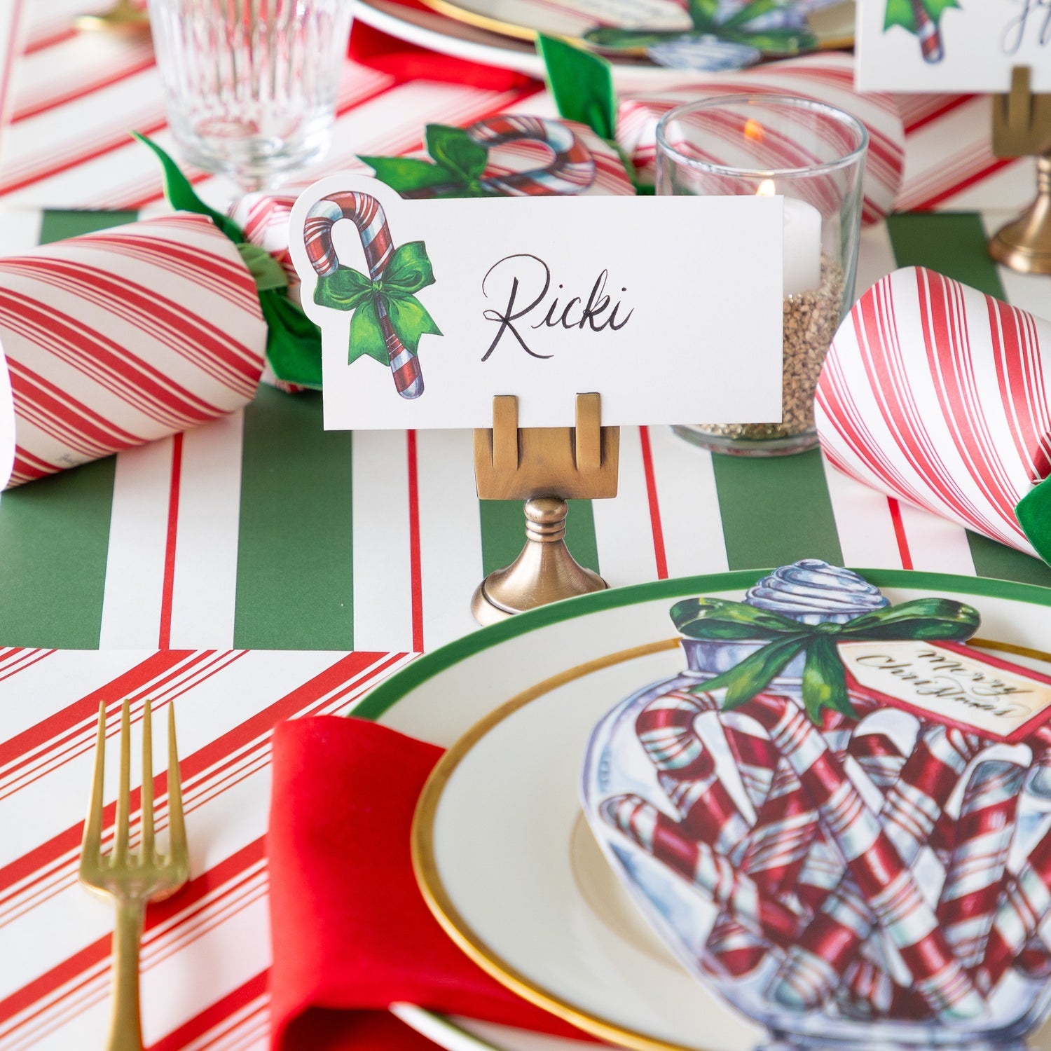 The Candy Cane Place Card reading &quot;Ricki&quot; held by the Brass Place Card Holder, behind a festive place setting.
