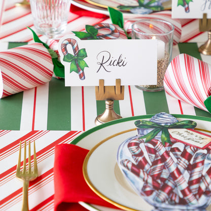 The Candy Cane Place Card reading &quot;Ricki&quot; held by the Brass Place Card Holder, behind a festive place setting.