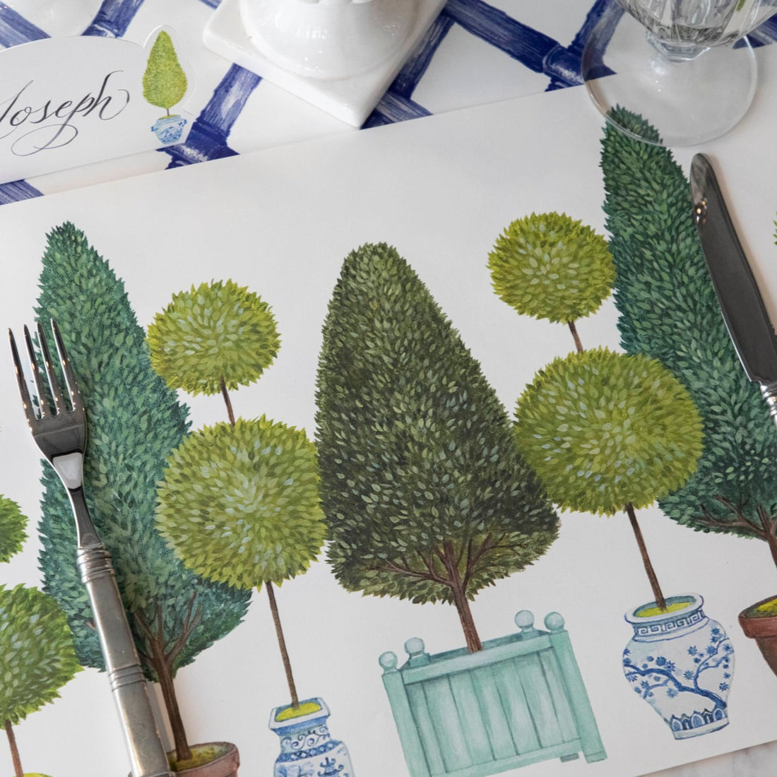 Close-up of the Topiary Garden Placemat in a place setting, showing the illustrated foliage in detail.