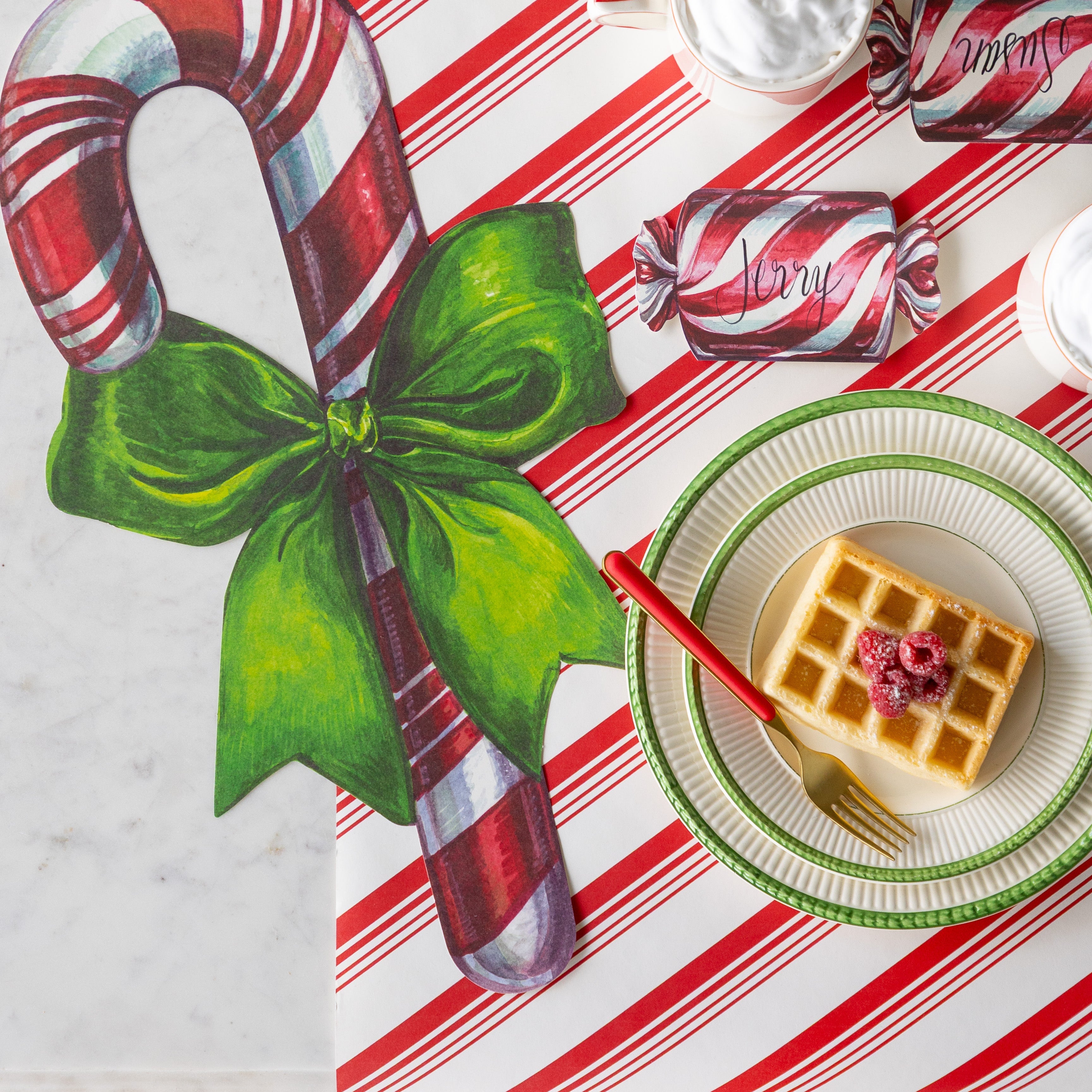 The Christmas Candy Place Card reading &quot;Jerry&quot; next to the Die-cut Candy Cane Placemat and behind two stacked plates with waffles and a fork on it.