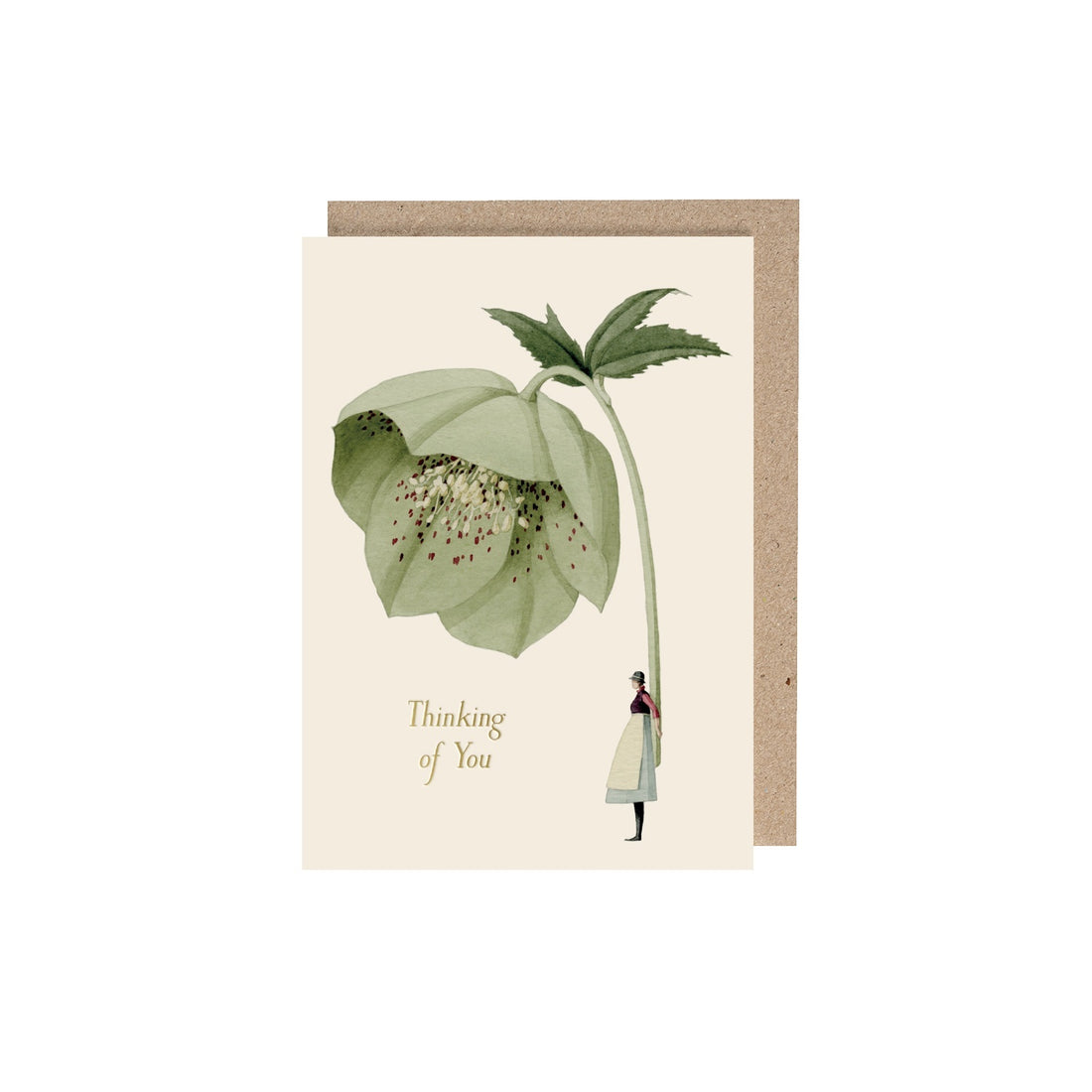 An off-white greeting card featuring a stylized illustration of a woman holding a gigantic green hellebore bloom by the stem, with the included kraft paper envelope and gold foil text that reads &quot;Thinking of you&quot;.