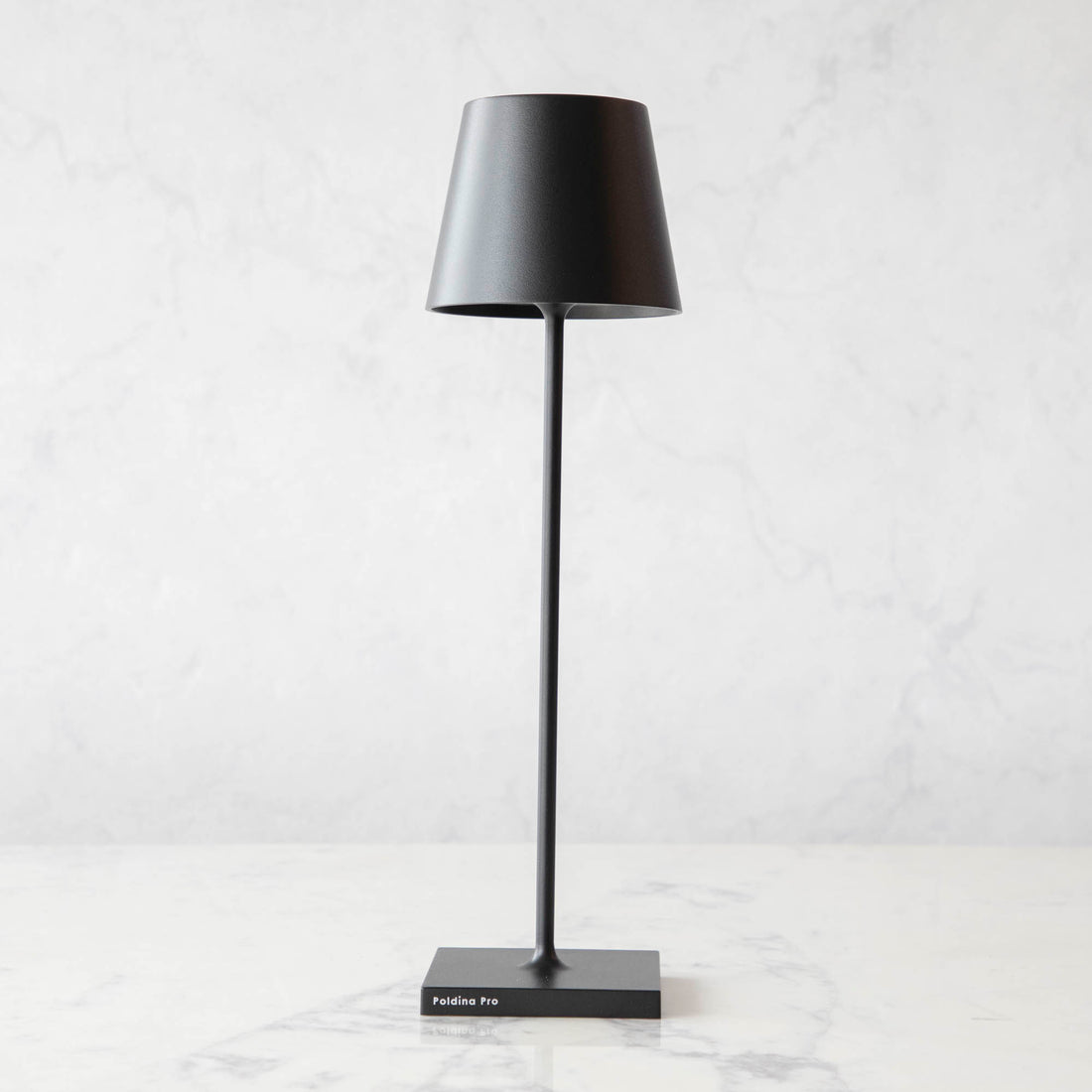 A Black Cordless Lamp by Zafferano on a table next to a book and a plant.