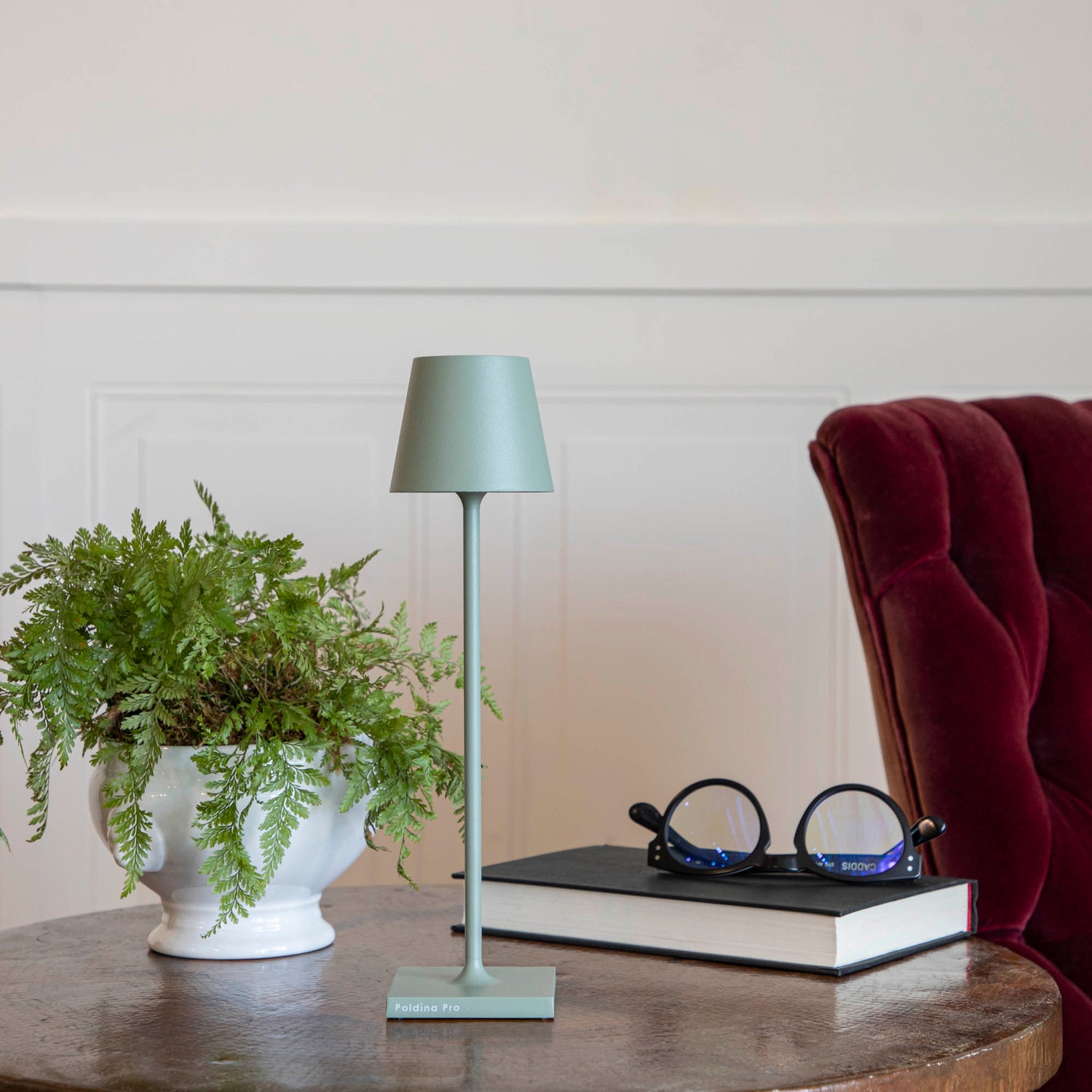 A Sage Micro Cordless Lamp by Zafferano on a table next to a book and a plant.
