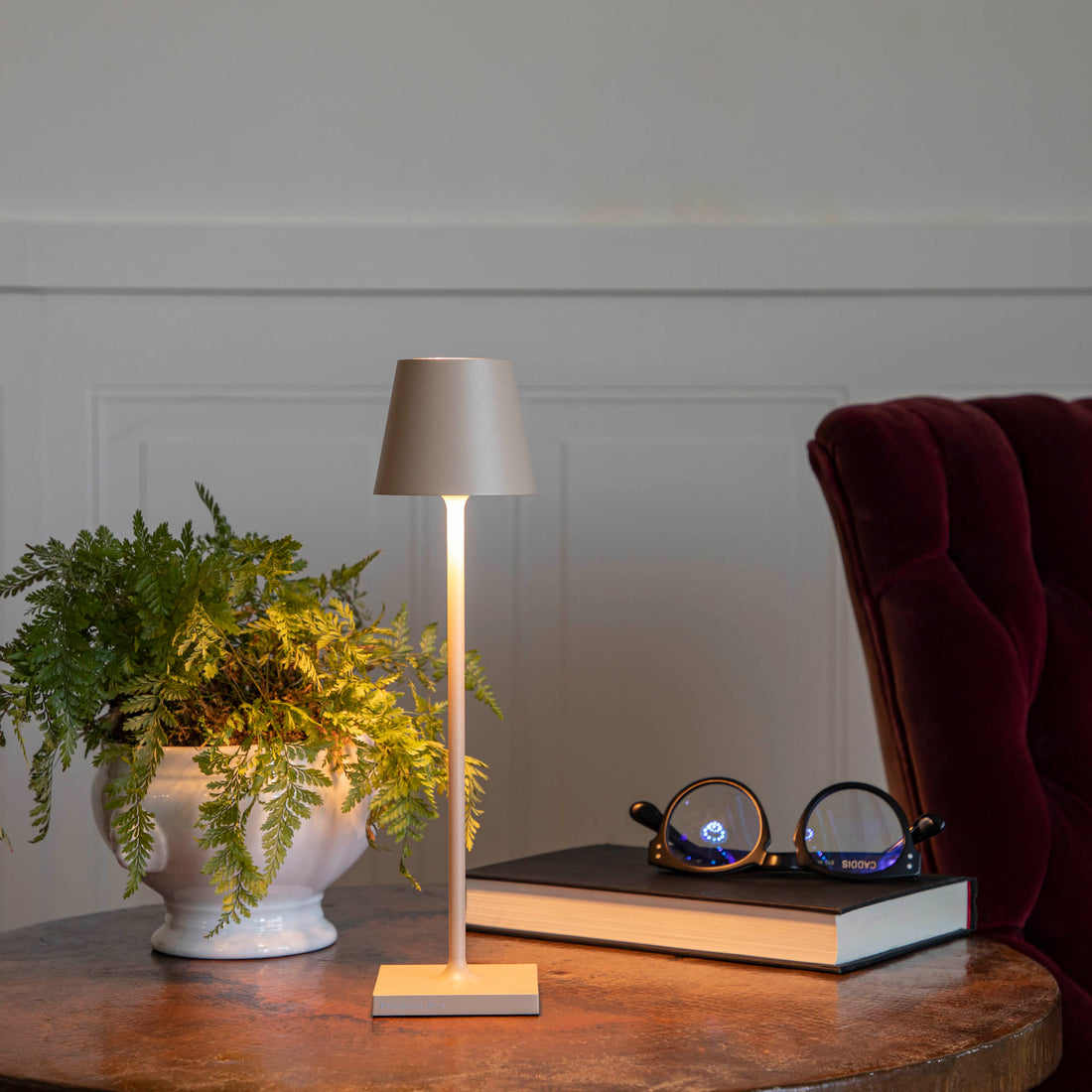 A Sand Micro Cordless Lamp by Zafferano on a table next to a book and a plant.