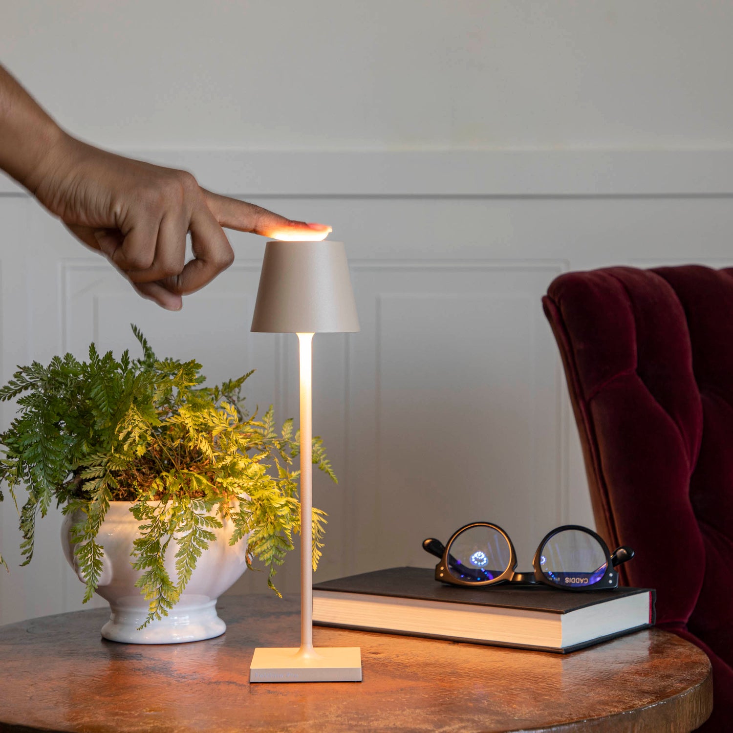 A Sand Micro Cordless Lamp by Zafferano on a table next to a book and a plant.