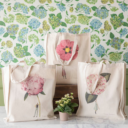 Three of the Heavyweight Canvas Tote Bags featuring pink floral artwork by Laura Stoddart arranged alongside potted plants against a hydrangea wallpaper background.