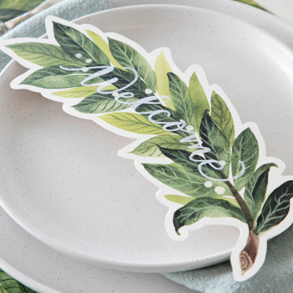 An elegant place setting featuring a Laurel Table Accent with &quot;Welcome&quot; written on it in white ink resting on the plate.