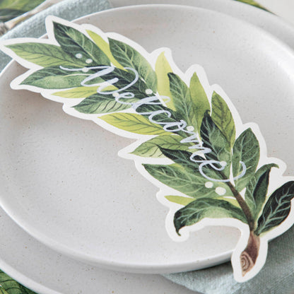 An elegant place setting featuring a Laurel Table Accent with &quot;Welcome&quot; written on it in white ink resting on the plate.