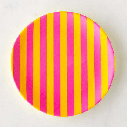 A round Stripe Melamine Plate with alternating vertical hot pink and yellow stripes on a marble table.