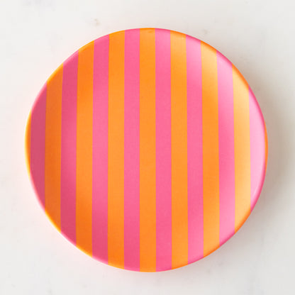 A round Stripe Melamine Plate with alternating vertical pink and orange stripes on a marble table.