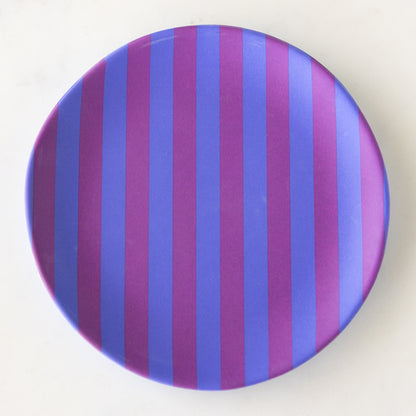 A round Stripe Melamine Plate with alternating vertical purple and blue stripes on a marble table.