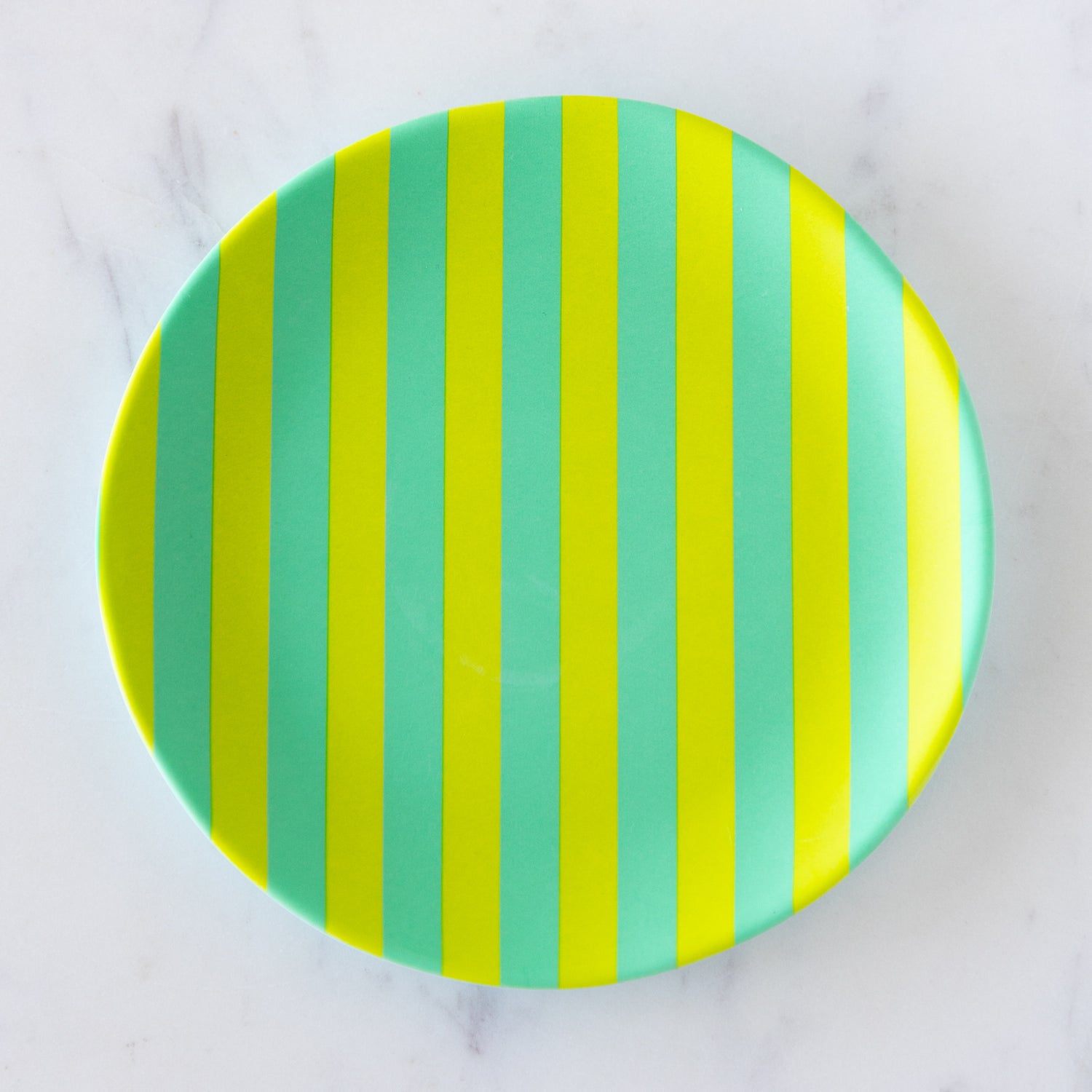 A round Stripe Melamine Plate with alternating vertical lime green and teal stripes on a marble table.