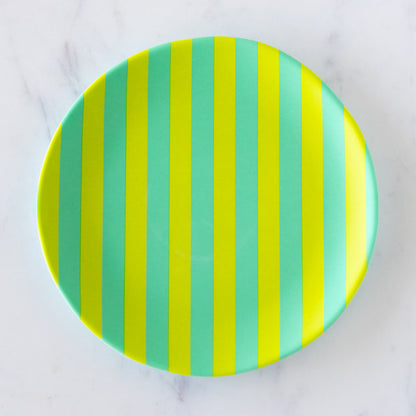 A round Stripe Melamine Plate with alternating vertical lime green and teal stripes on a marble table.