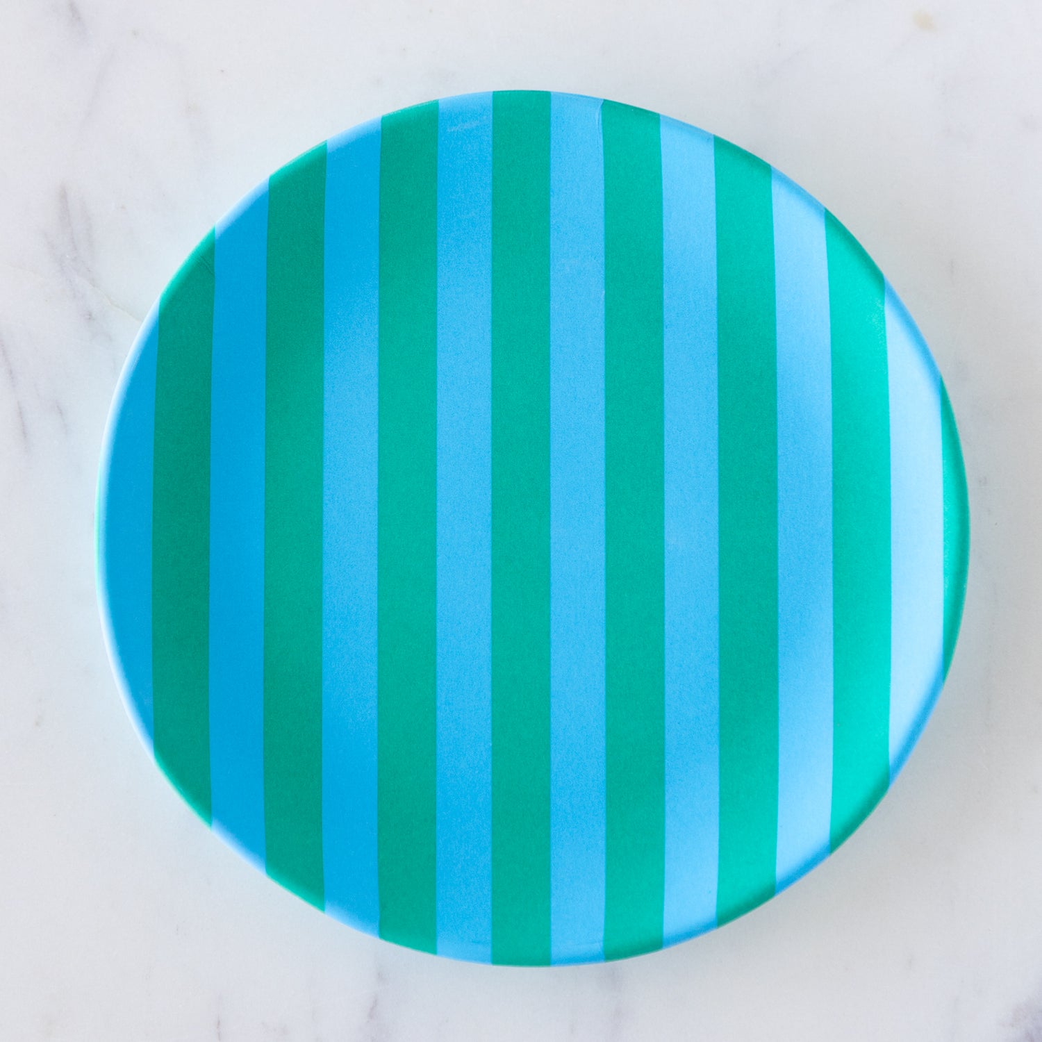A round Stripe Melamine Plate with alternating vertical light blue and turquoise stripes on a marble table.