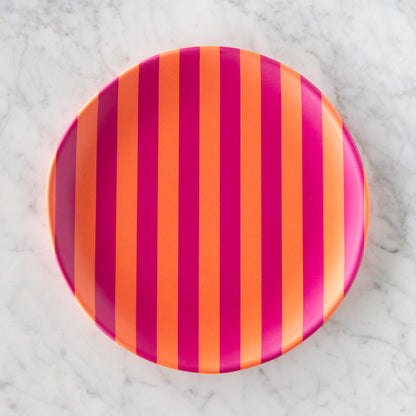 A round Stripe Melamine Plate with alternating vertical orange and magenta stripes on a marble table.
