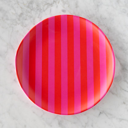 A round Stripe Melamine Plate with alternating vertical hot pink and red stripes on a marble table.