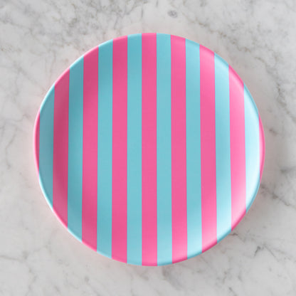 A round Stripe Melamine Plate with alternating vertical pink and light blue stripes on a marble table.