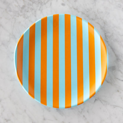 A round Stripe Melamine Plate with alternating vertical light blue and orange stripes on a marble table.