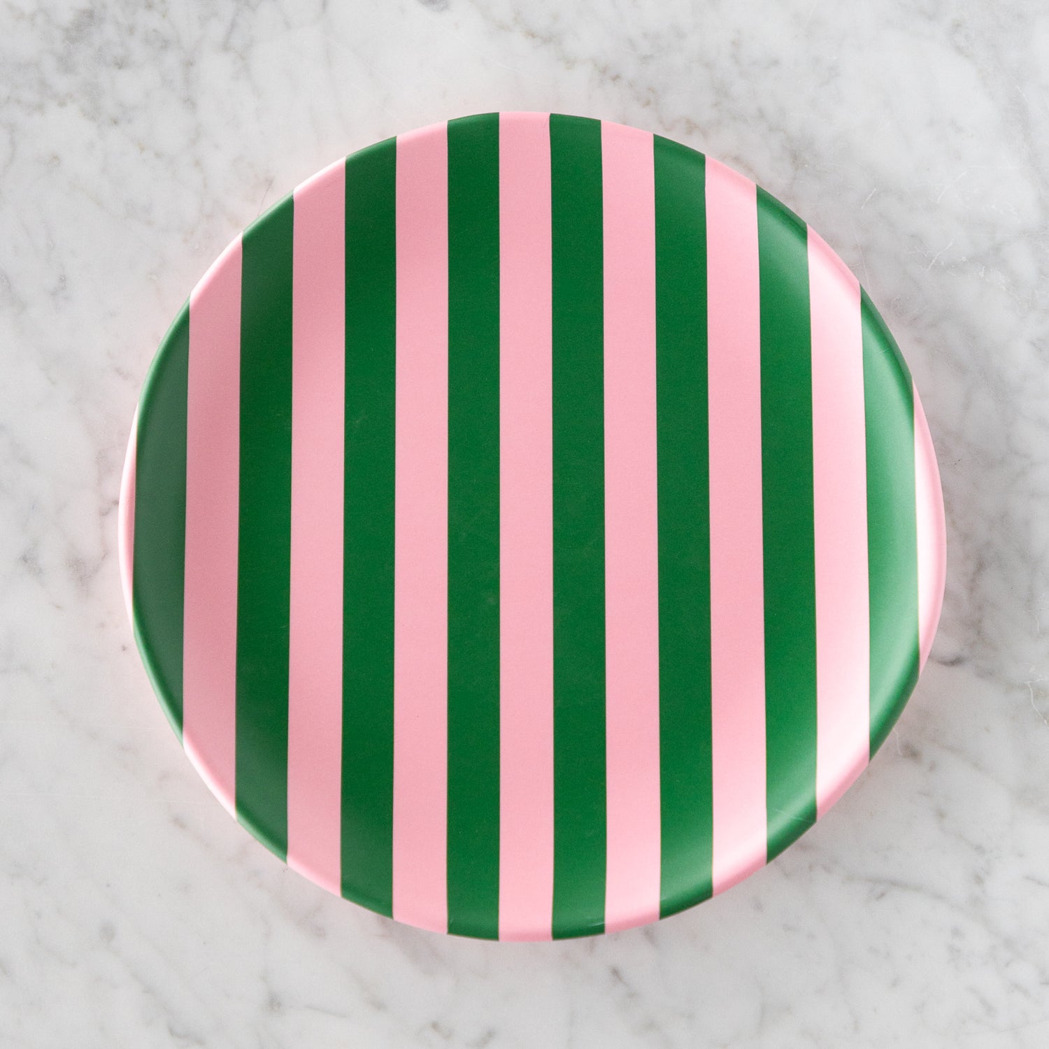 A round Stripe Melamine Plate with alternating vertical pink and green stripes on a marble table.