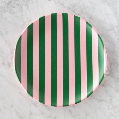 A round Stripe Melamine Plate with alternating vertical pink and green stripes on a marble table.
